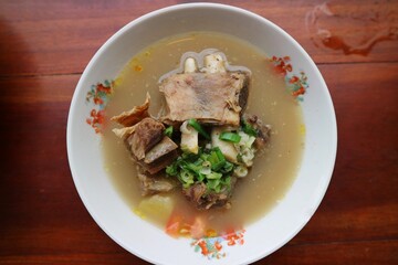 Sop Iga Sapi in white bowl on the wooden table. Beef Rib Soup is typical Indonesian dish, made from mixing beef ribs, carrots, leeks and celery. Selective focus.