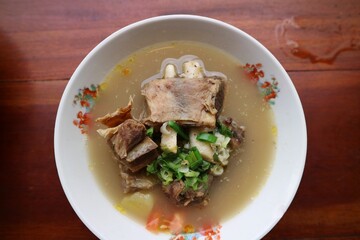 Sop Iga Sapi in white bowl on the wooden table. Beef Rib Soup is typical Indonesian dish, made from mixing beef ribs, carrots, leeks and celery. Selective focus.