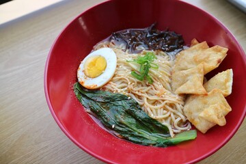 Gyoza dumplings and Ramen in the re bowl on the wooden table. Served with boiled egg, vegetable and...