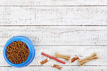 Dry pet food in bowl with bones on white wooden table