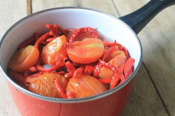 Chili, tomatoes and onions stewed in a red pot on the table