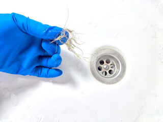 Removing Hair Clog From a Bathroom Sink Drain. Gloved hand extracting hair from a sink