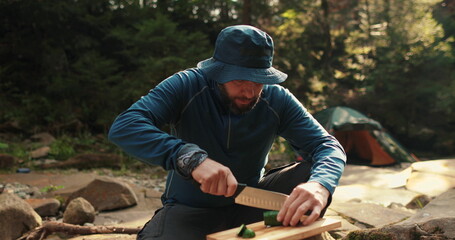 A man cooks food outdoors on a camping trip while sitting by a campfire. Cooking food on a tourist trip to the mountains. Camping and outdoor cooking.