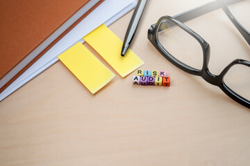 Concept on Business and Risk Audit. Colorful cubes with RISK AUDIT words on the desk. A pen, eyeglasses, and notebook at the side