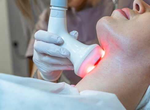 Photo from studio of cosmetology, demonstrating process of led therapy and facial skin care. Woman undergoes procedure in beauty salon. Beautician in white gloves use cosmetologic laser device