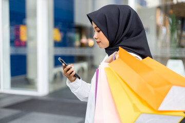 Muslim women wear hijab holding smartphone shopping bag color in supermarket. Female islamic arabic...