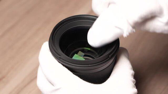A Specialist cleaning the front glass element of a digital photo lens using cleaning cloth and a dust blower