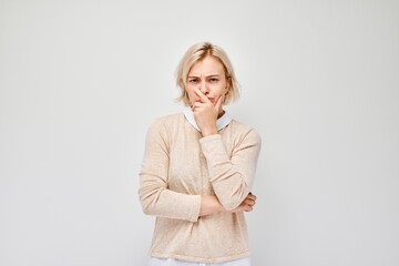 Woman pondering with hand on chin, looking uncertain, against a white background. - obrazy, fototapety, plakaty