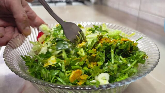 white hands mixing vegetable salad with mayonnaise in a glass bowl with a stainless steel fork at domestic kitchen