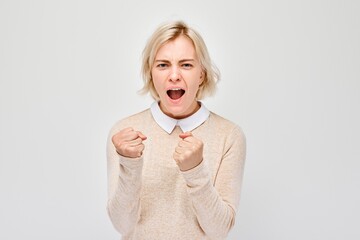 Portrait of an angry blond woman clenching her fists and yelling on a white background