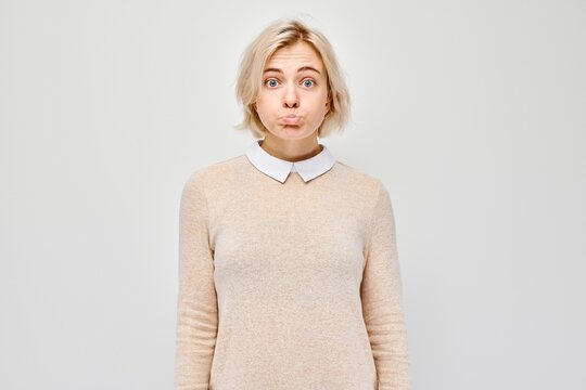 Surprised young woman with a funny expression, standing against a light grey background.