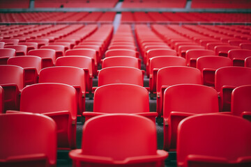 Football stadium with empty seats. Outstanding empty red plastic chair at soccer arena. Row of unoccupied bench at sports stadium. Reserved seating for football game concept. Outdoor audience chairs - obrazy, fototapety, plakaty