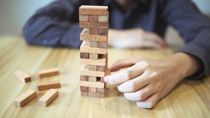 Business strategy concept with hands playing a wooden block tower game, symbolizing risk and stability. Planning risk management