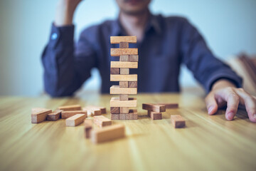 Business strategy concept with hands playing a wooden block tower game, symbolizing risk and...
