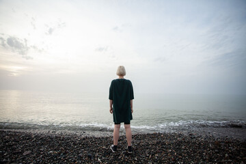 Girl alone. Young woman with short blonde bob hair and green dress on cold sea beach