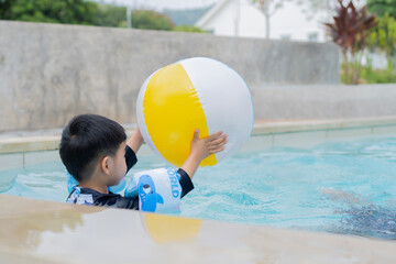 Little Asian boy in the pool with a life buoy on his arms and playing a beach boy