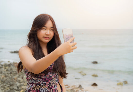 Portrait picture of happy Asian young woman with mobile phone on a beach