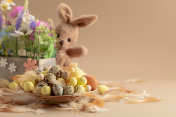 Easter eggs, feathers, spring flowers, and toy bunny on a beige background.
