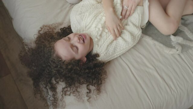 Caucasian mother tickling little happy carefree cheerful laughing kid daughter resting together on comfortable couch at home. Mom holding child girl upside down tickle joyful sincere family having fun