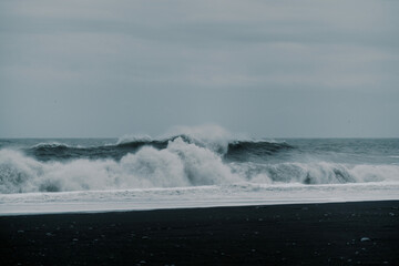 Naklejka premium Waves crash against contrast black sand rock beach Icelandic nature