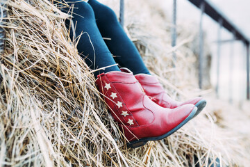 Child wearing red cowboy boots with stars sitting on haybale © Cavan