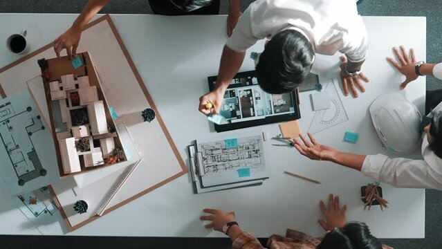 Top down view of architect engineer team discussing and point at tablet display construction at table with blueprint and house model at meeting. Diverse designer planning design house. Alimentation.