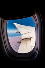 Aerial view of clouds and blue sky from window of airplane.   Airplane wing against the blue sky from the porthole. 