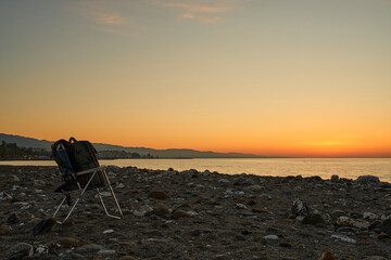 Fototapeta na wymiar amanecer en la playa con una silla y una mochila