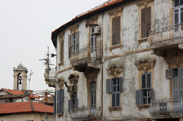 Fototapeta na wymiar Bell Tower of The Greek Orthodox Church with Cross and Abandoned Greek Home with Shutters and Balconies in Hatay, Turkey