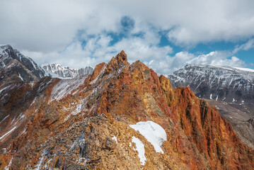 Vivid sharp pinnacle in sunlight. Shiny pointy peak of gold color. Colorful red rocky peaked top. Freshly fallen snow in high mountains. Sunny cloudy alpine view. Snowy cornice on stony mountain ridge
