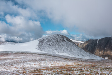 Awesome landscape with most beautiful rocky hill in freshly fallen snow among high mountains under cloudy sky. Colorful alpine view to snowy stony pass and wide snow-white glacier among low clouds.