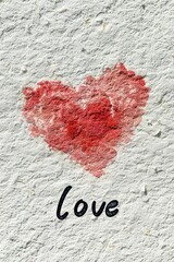 A rough red heart and the word love painted on a textured white wall.