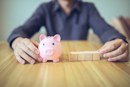 A person with a piggy bank and wooden blocks on a table, illustrating concepts of savings and investment