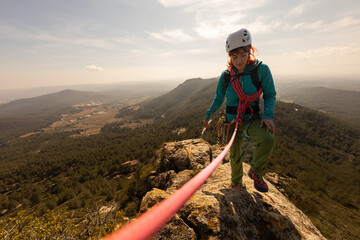 A woman is climbing a mountain with a red rope. She is wearing a helmet and a blue jacket. The...