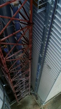 Metal brown tower with tube inside attached to a silo tank and warehouse. Descending footage along the granary premises. Top view. Vertical video