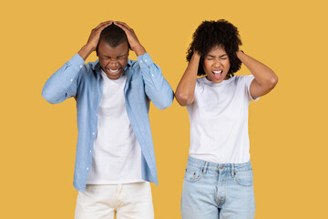 Stressed young couple with hands on their heads, eyes closed, and faces contorted in frustration