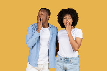 A young couple in casual clothes looking tired and bored, yawning with hands over their mouths