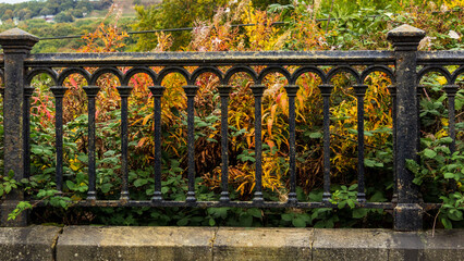 A old but sturdy crafted iron boundary fence against the background of autumn colours in the Unesco World Heritage site model village of Saltaire in West Yorkshire