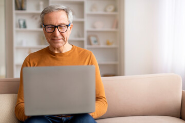 Grandfather wearing eyeglasses using laptop at home