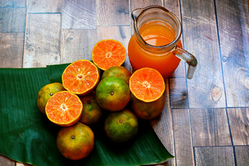 Fresh orange fruit on the banana leaf with orange juice in the glass pitcher on wooden table