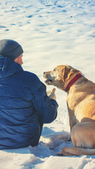 A man with a dog sits on a snowy field in winter back to the camera. Vertical banner - 760473911