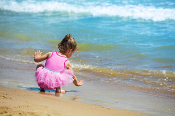 Little girl sits with her back to the camera on the beach and plays with water - 760473941