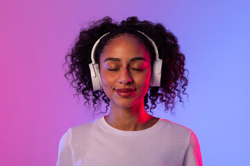Content black lady with headphones enjoying music on neon background