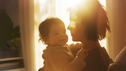 Lovely intimate home scene of a mother and her baby son in her arms. Quiet moment of love and pure feelings between mom and child with warm light