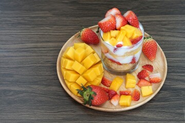 Fresh ripe mango, and strawberry fruit in a cup with cookies, and soy yogurt on a wooden plate and wooden background
