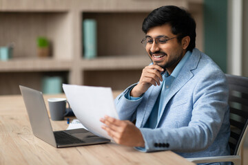 Contented Indian businessman looks through papers engrossed in work indoor