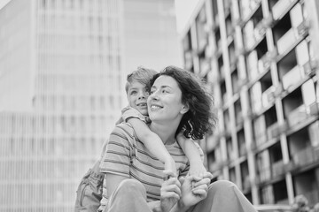 young mother and son smiling looking at the camera in modern residential complex. Having fun together, happy parenting, new home concept. Bright summer day in the urban background. High quality photo