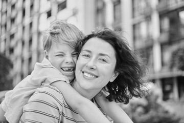 young mother and son smiling looking at the camera in modern residential complex. Having fun together, happy parenting, new home concept. Bright summer day in the urban background. High quality photo