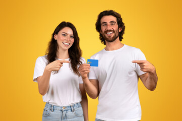 Smiling young couple in casual white t-shirts, the woman pointing at a blue credit card