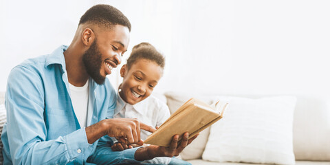 Caring african-american daddy reading book to his cute daughter